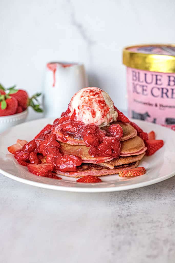 plated strawberry pancakes with fresh strawberries and a pint of ice cream in the background
