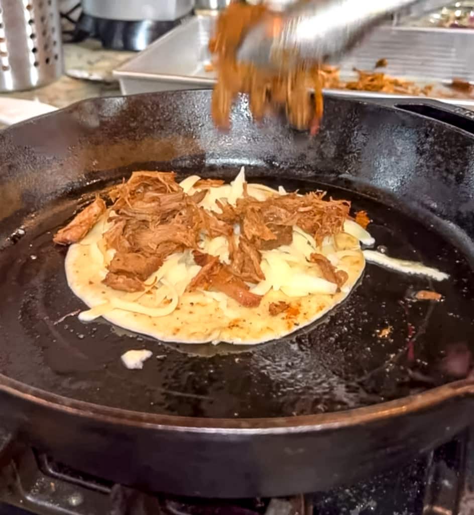 adding carnitas to corn tortillas in cast iron skillet for tacos