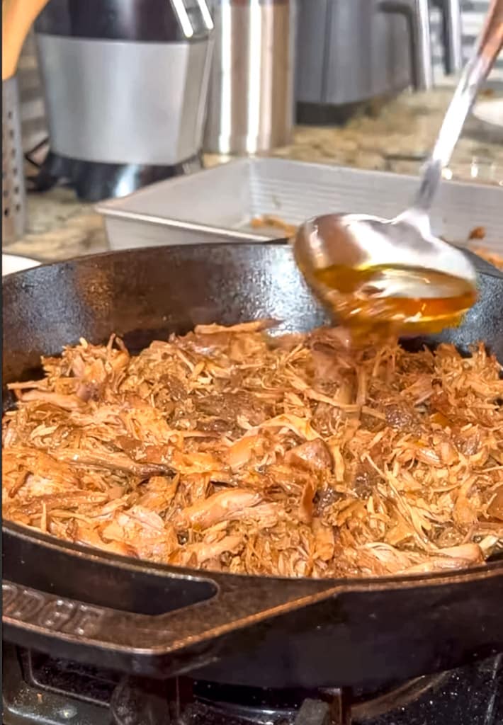 adding sauce to carnitas in a skillet