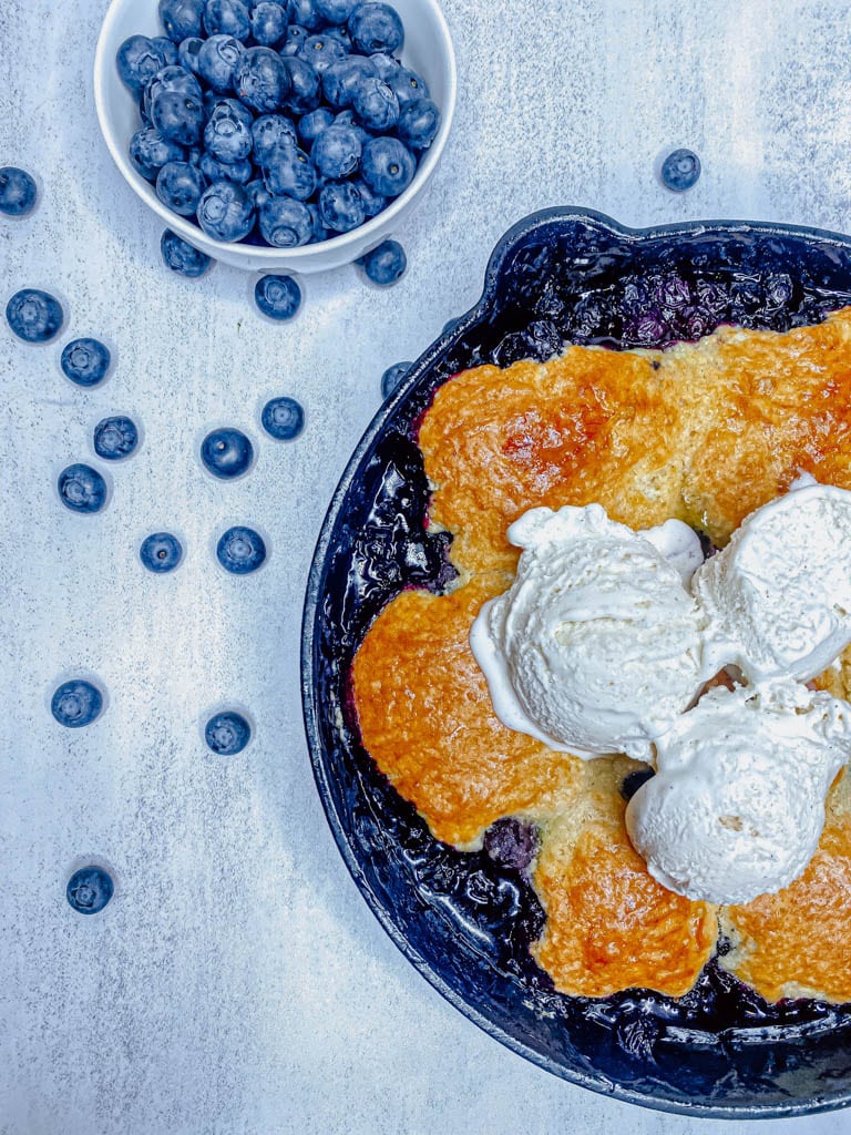 half a skillet of blueberry cobbler with blueberries scattered around