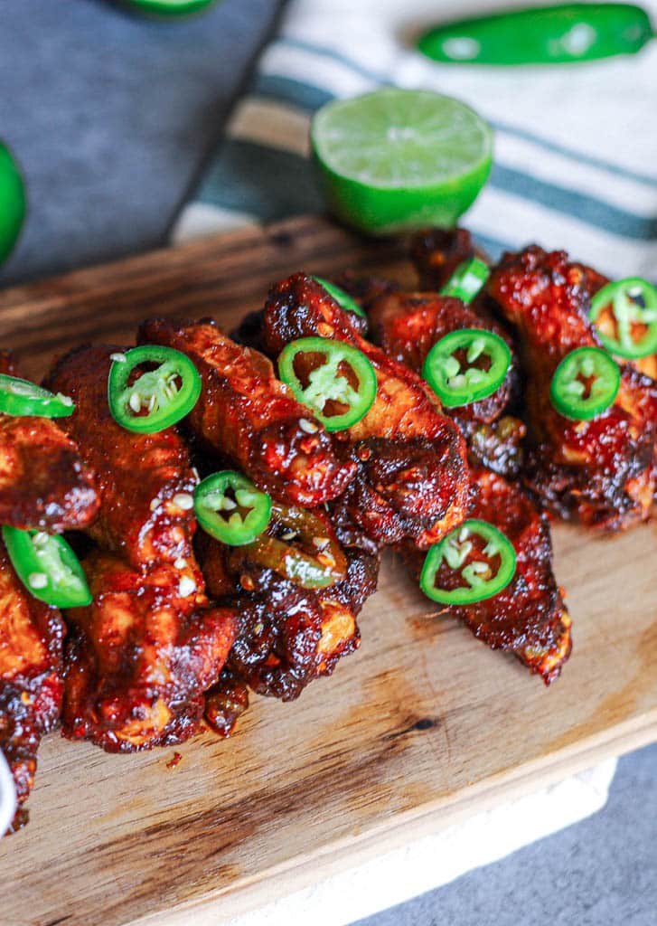 a wooden cutting board with a stack of chili lime wings on it and sliced jalapenos
