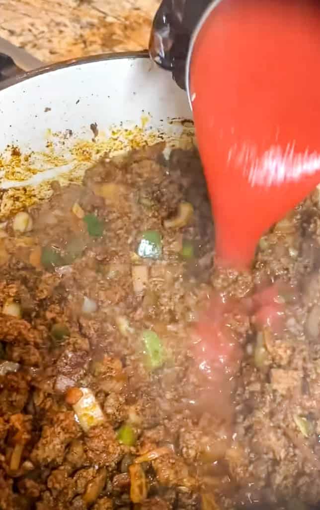 tomato sauce being added to the texas chili mixture