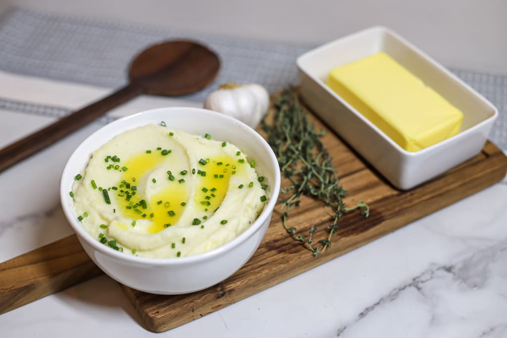 Buttery Mashed Potatoes in a white bowl with chives sprinkled on top