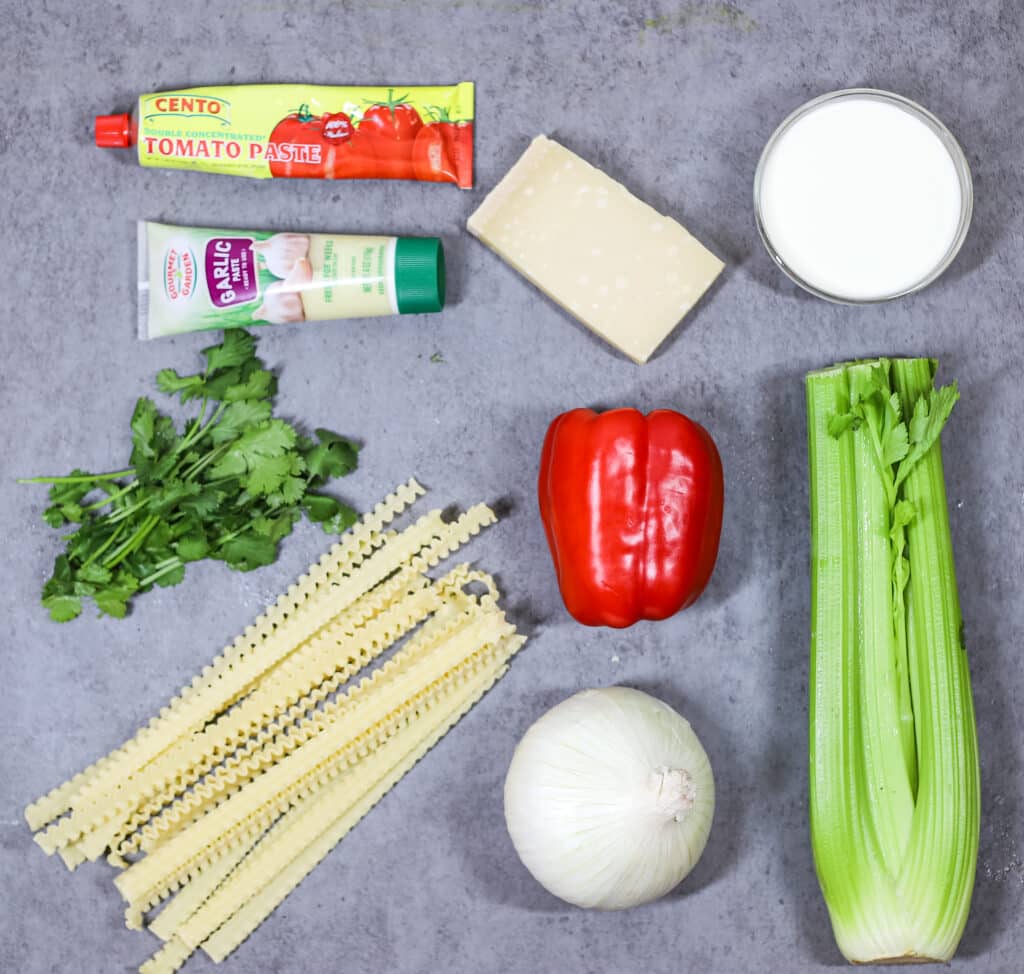 ingredient over-head shot: tomato paste, garlic paste, parsley, noodles, parmesan cheese, red bell pepper, white onion, heavy cream, bunch of celery