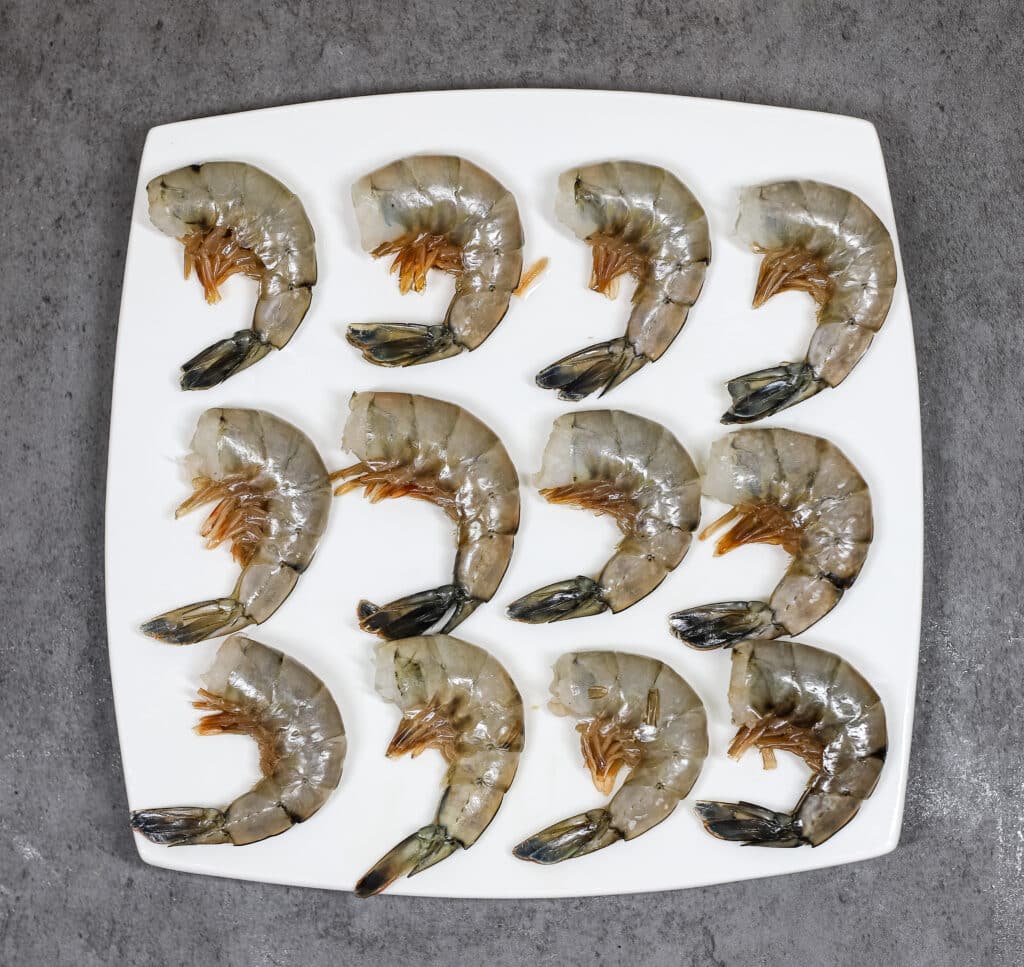 twelve raw shrimp on white plate