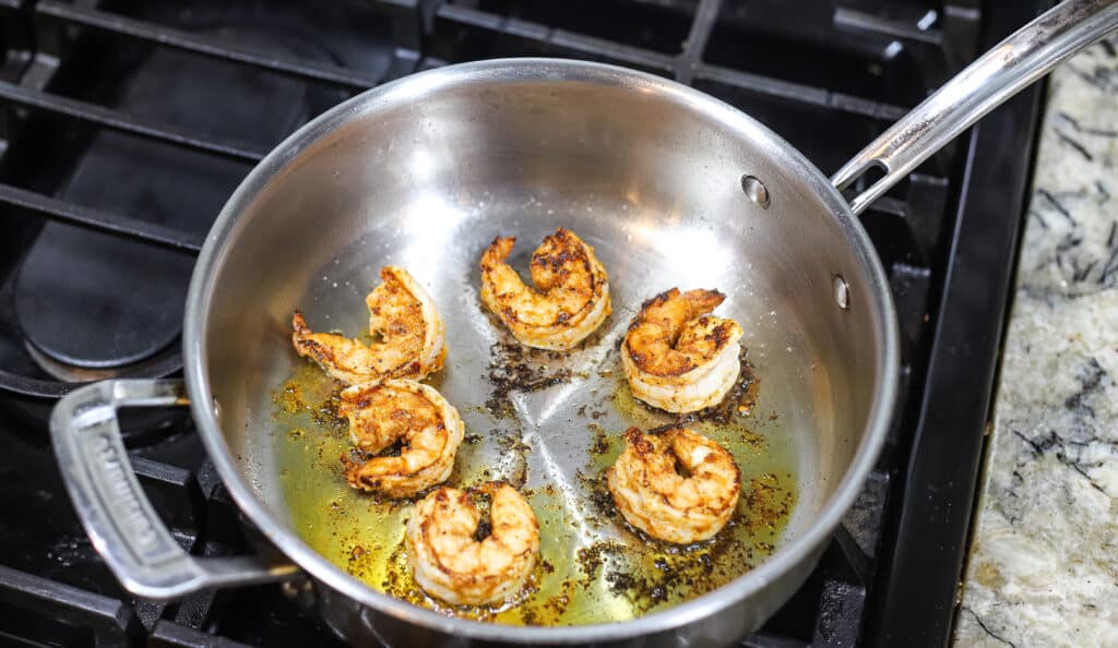 six shrimp sautéed in oiled skillet on stovetop