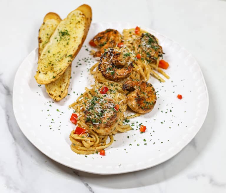 cajun shrimp pasta plated with two pieces of garlic bread on plate