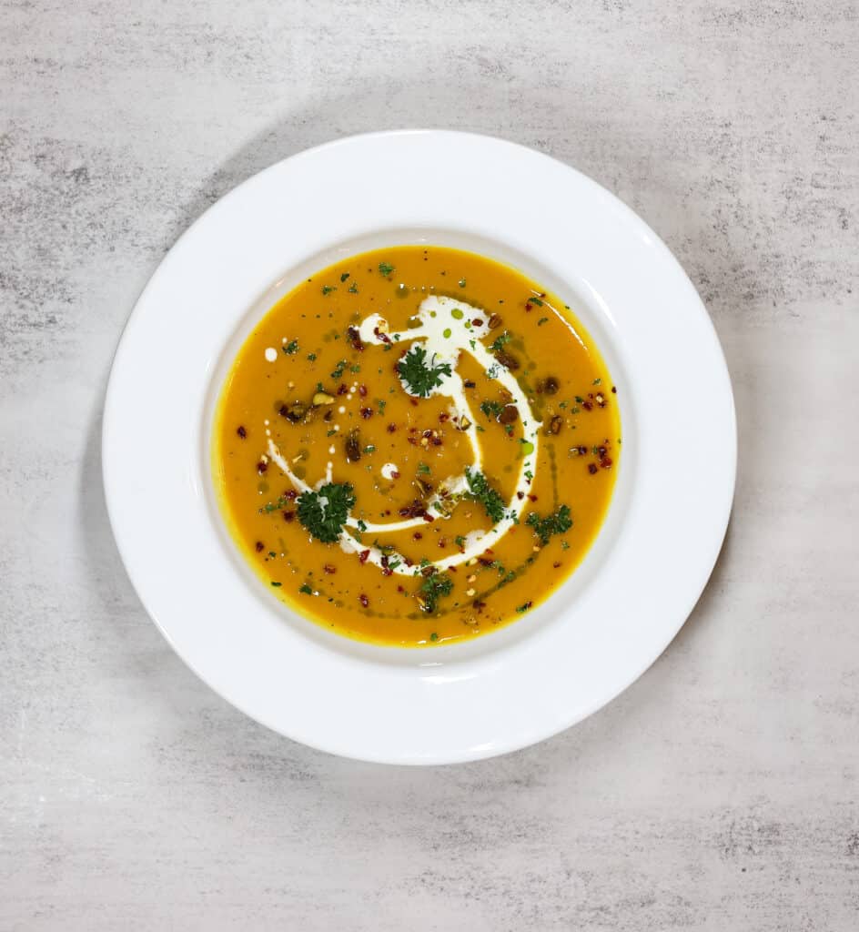 Roasted butternut squash soup in white bowl garnished with parsley, greek yogurt, and red pepper 