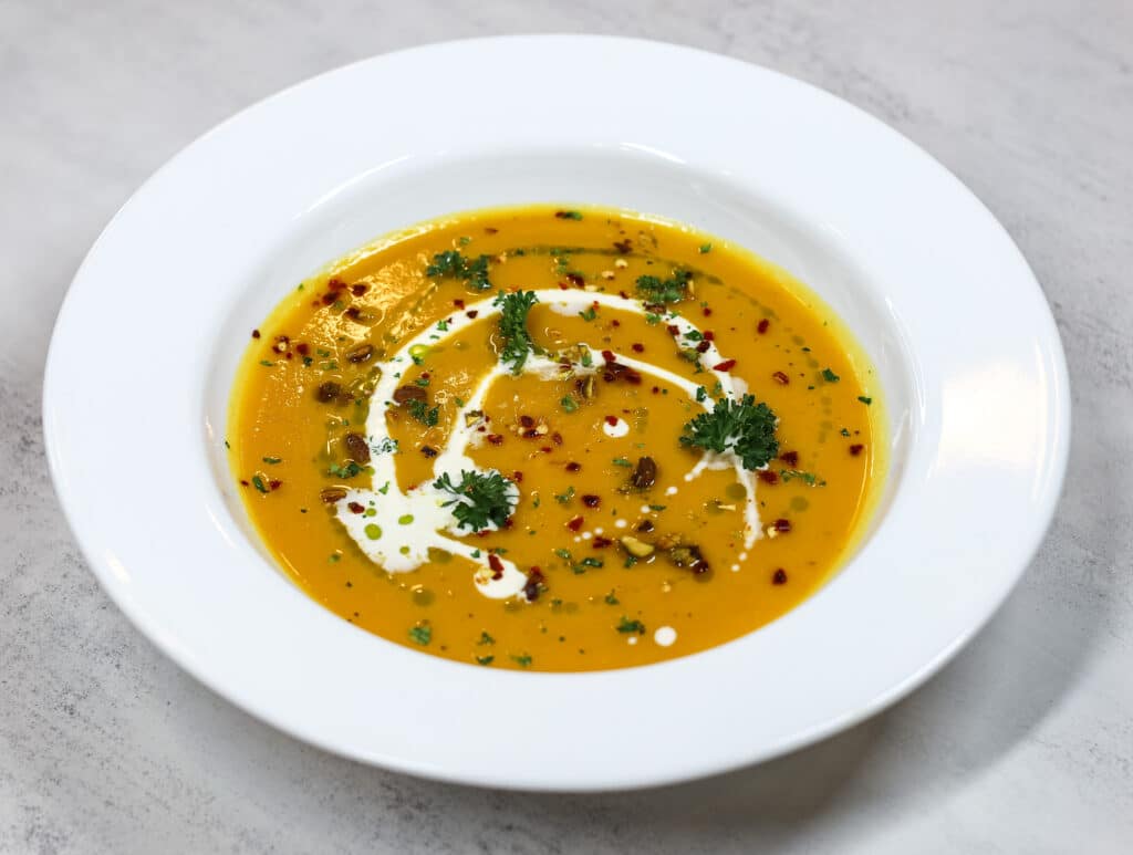 Roasted butternut squash soup in white bowl garnished with Greek yogurt, parsley, and red pepper flakes