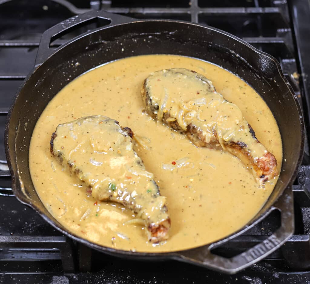 2 pork chops smothered in gravy in cast iron skillet on stovetop