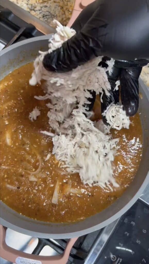 adding shredded chicken to sauce to make the chicken Tinga