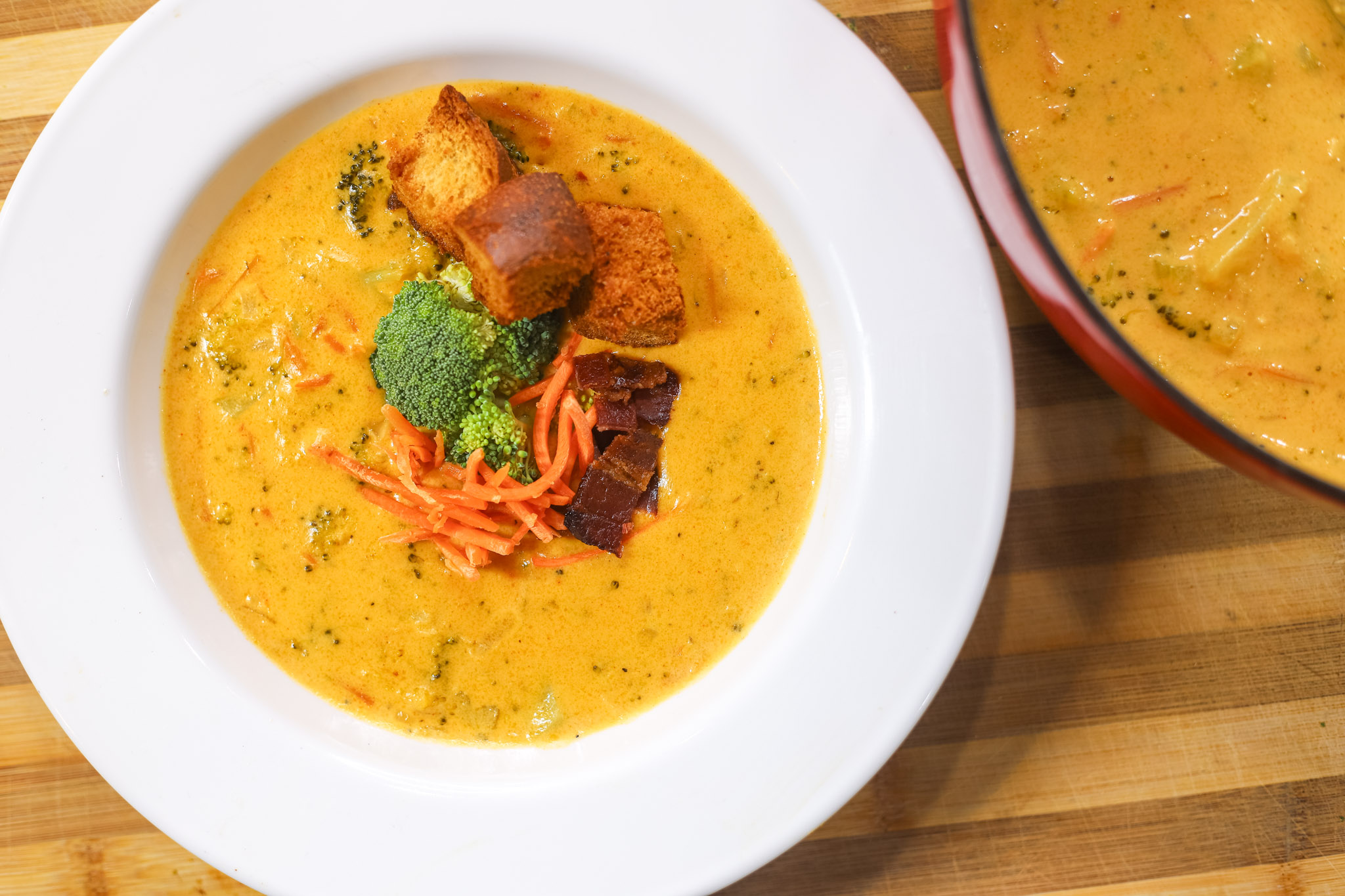 Broccoli Cheddar Soup topped with bacon, broccoli, carrots, and french bread