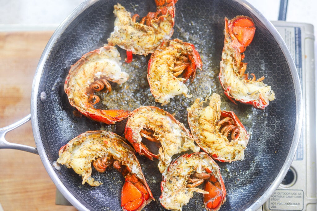 Halved lobster tails cooking meat-side down in melted butter